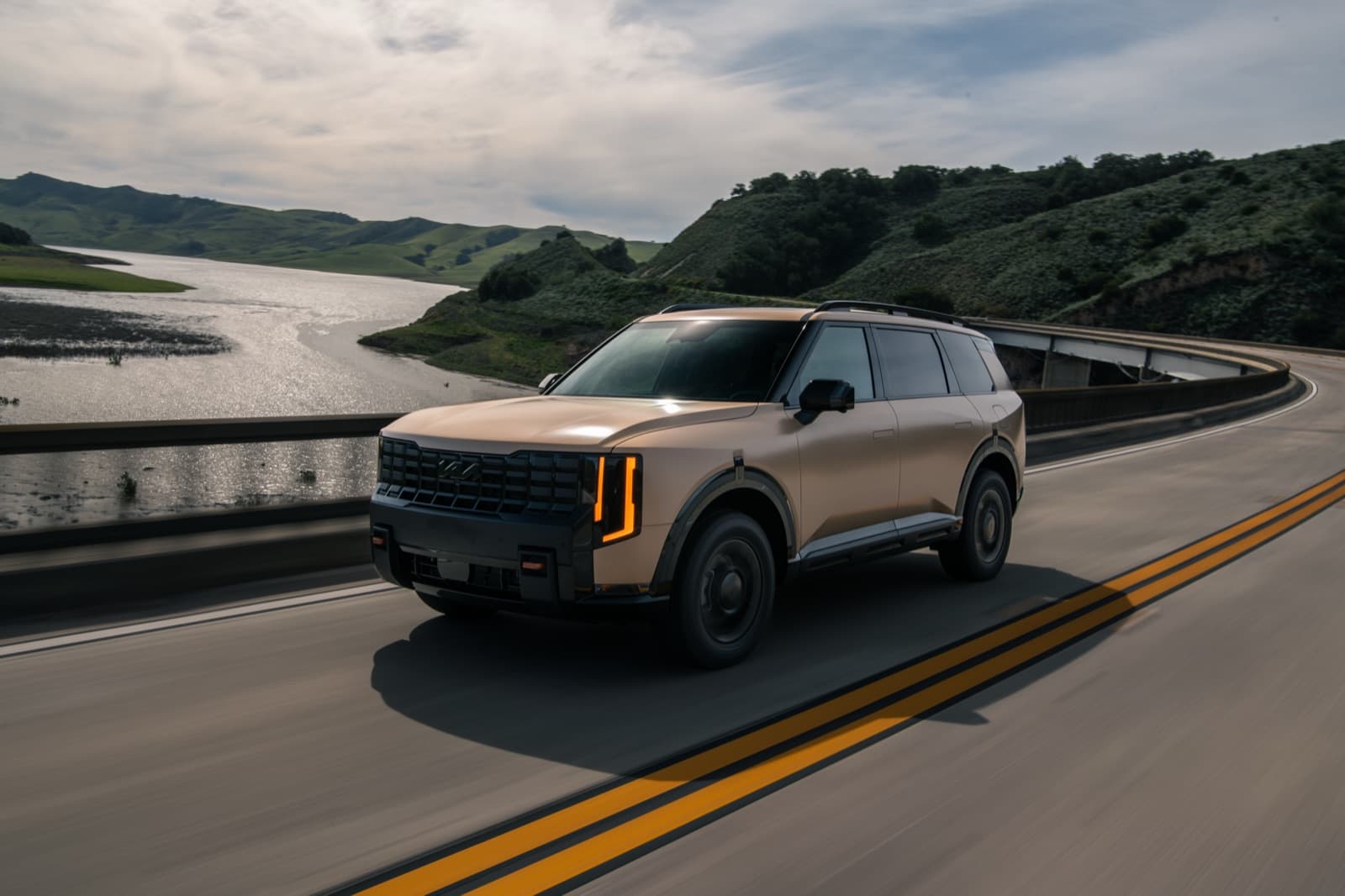 2027 Kia Telluride driving across a coastal bridge, front three-quarter view